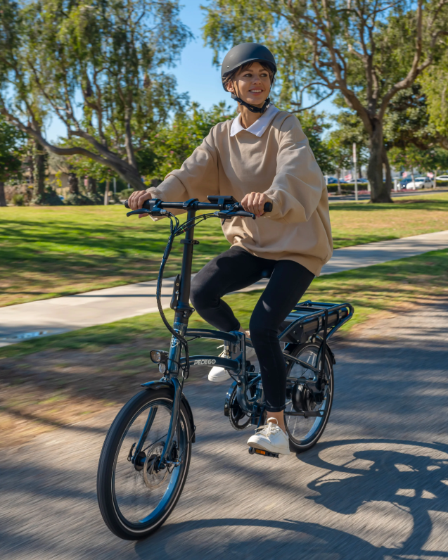 Person riding a electric Pedego Latch folding bike on a path with trees and grass in the background